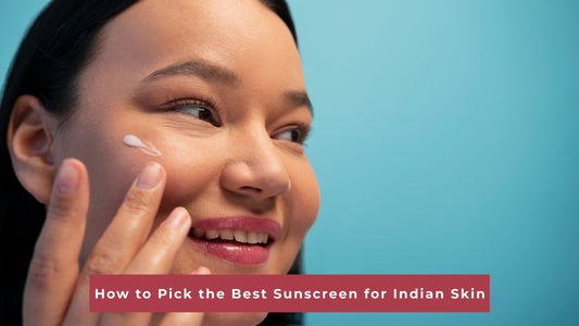 A smiling woman applying a small dab of white cream to her cheek against a solid turquoise blue background, with a text overlay at the bottom that reads "How to Pick the Best Sunscreen for Indian Skin.